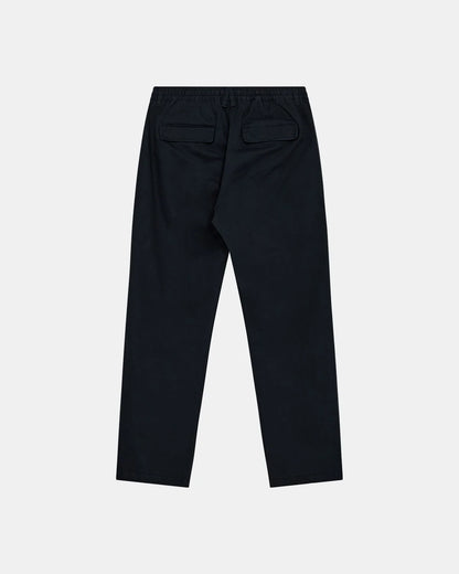 Vista frontale flat lay dei pantaloni Anerkjendt AKJAN Cotton Pleat Ela Pants in Navy Blue su sfondo grigio chiaro: pantaloni uomo vita elastica con coulisse laccetto scuro doppia pinces frontale tasche laterali a filetto e gamba tapered con patch etichetta rotonda Anerkjendt sulla vita