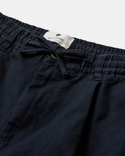 Vista posteriore flat lay dei pantaloni Anerkjendt AKJAN Cotton Pleat Ela Pants in Army Green Olive su sfondo grigio chiaro: retro dei pantaloni uomo con vita elasticizzata due tasche posteriori con pattina e gamba tapered in cotone verde oliva