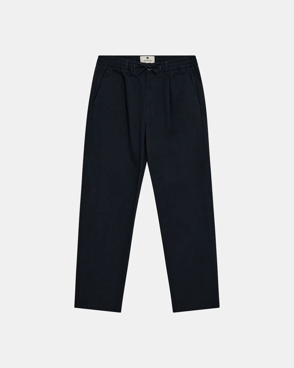 Vista frontale flat lay dei pantaloni Anerkjendt AKJAN Cotton Pleat Ela Pants in Navy Blue scuro su sfondo grigio chiaro: pantaloni uomo vita elasticizzata con coulisse laccetto nero doppia pinces frontale tasche laterali a filetto gamba tapered e patch etichetta rotonda Anerkjendt