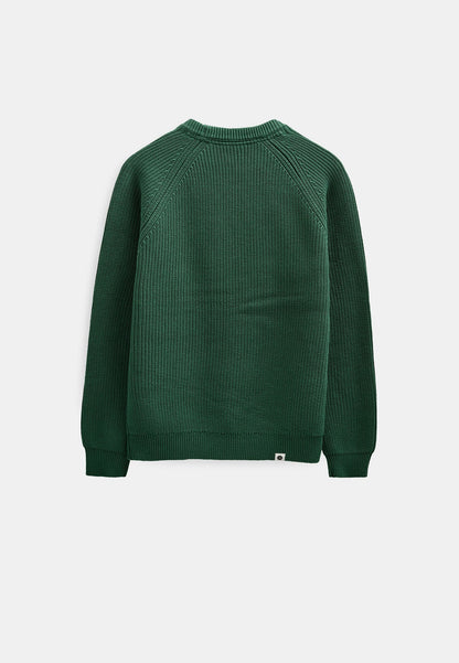 Dettaglio ravvicinato del petto e della spalla raglan del maglione Anerkjendt AKSUNE Patent Knit rosso bordeaux indossato dal modello: zoom sulla texture a costine verticali fitte e sulla cucitura raglan diagonale che parte dal collo