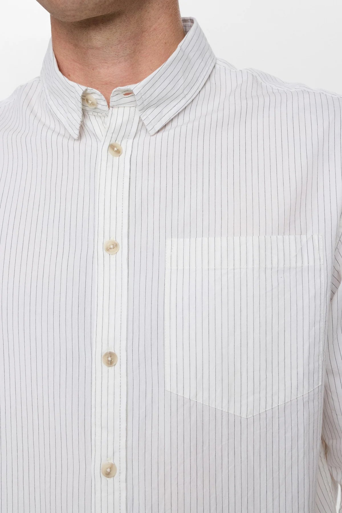 Dettaglio frontale ravvicinato della Anerkjendt AKOTTO Poplin Stripe LS Shirt Bright White indossata dal modello: zoom su colletto button-down aperto bottoni perlati e tasca a toppa con tessuto popeline a righe grigio-blu su fondo bianco avorio