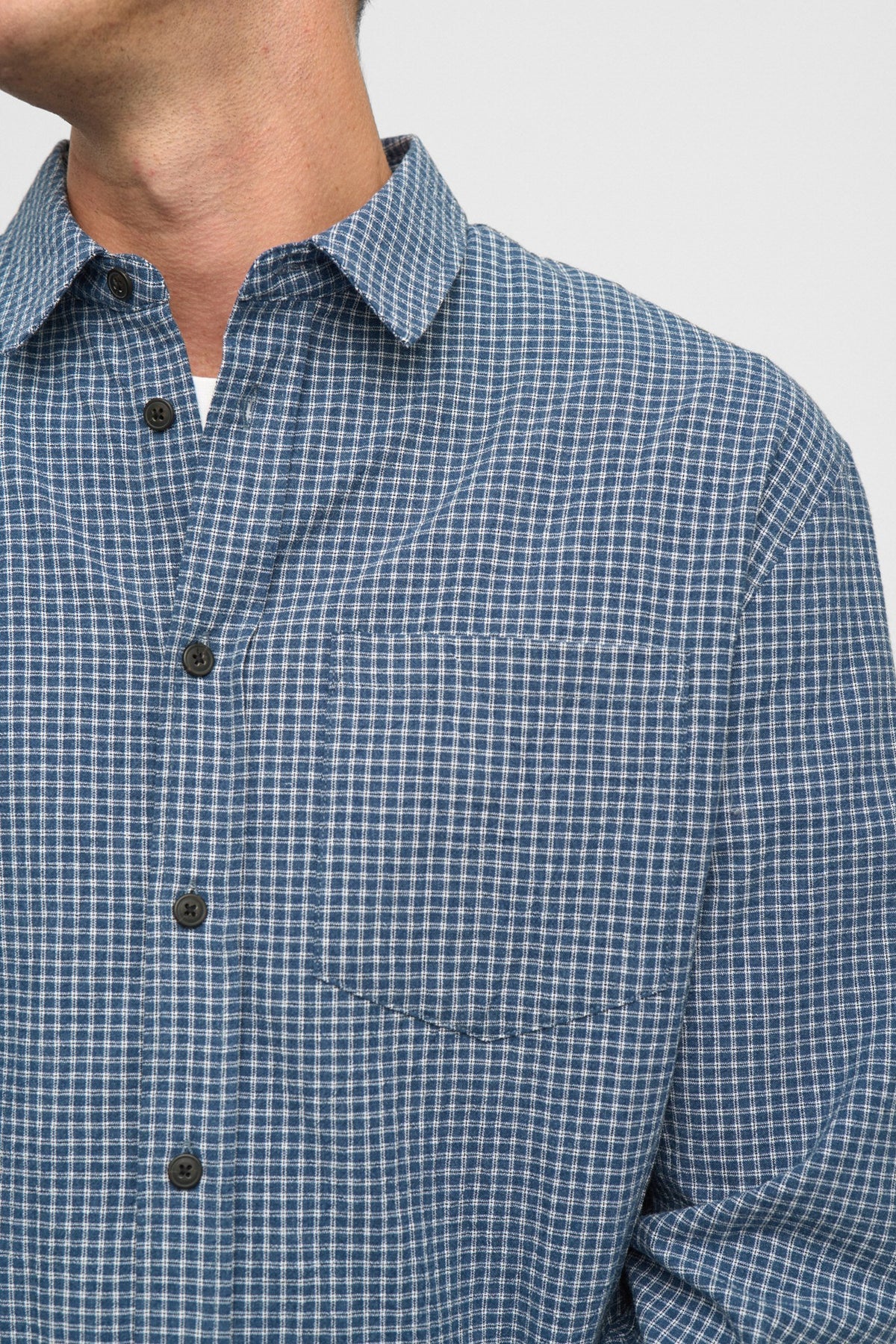 Vista frontale flat lay della Anerkjendt AKOTTO Small Check LS Shirt Estate Blue: camicia uomo a micro quadri blu navy e bianco con colletto classico, bottoni scuri, tasca a toppa sul petto e polsini a doppio bottone su sfondo grigio chiaro