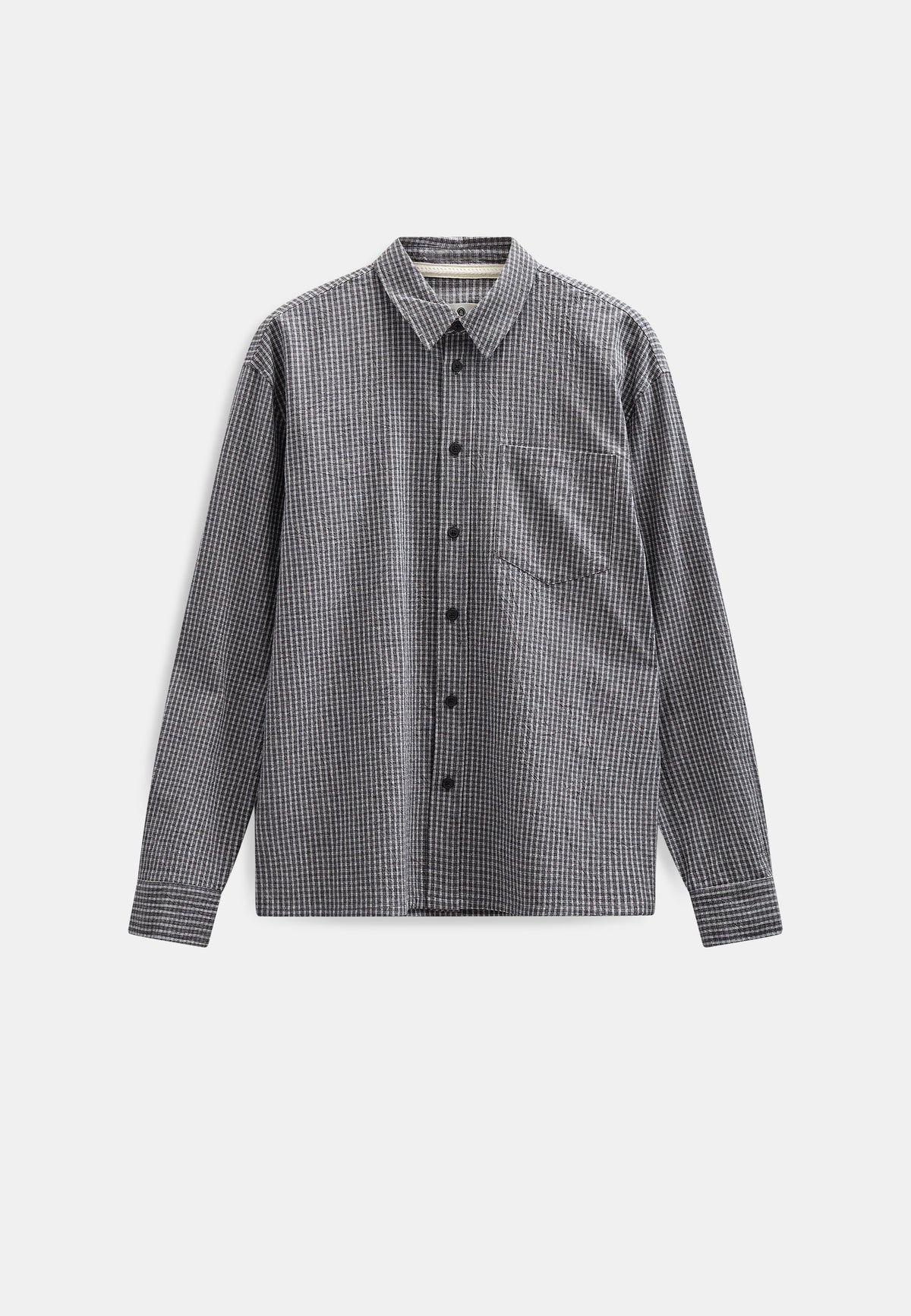 Vista frontale flat lay della Anerkjendt AKOTTO Small Check LS Shirt in colorazione Black Grey: camicia uomo a micro quadri grigio scuro e antracite con colletto classico bottoni scuri tasca a toppa sul petto e polsini con etichetta Anerkjendt visibile su sfondo grigio chiaro