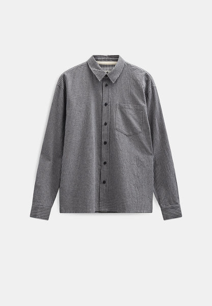 Vista frontale flat lay della Anerkjendt AKOTTO Small Check LS Shirt in colorazione Black Grey: camicia uomo a micro quadri grigio scuro e antracite con colletto classico bottoni scuri tasca a toppa sul petto e polsini con etichetta Anerkjendt visibile su sfondo grigio chiaro