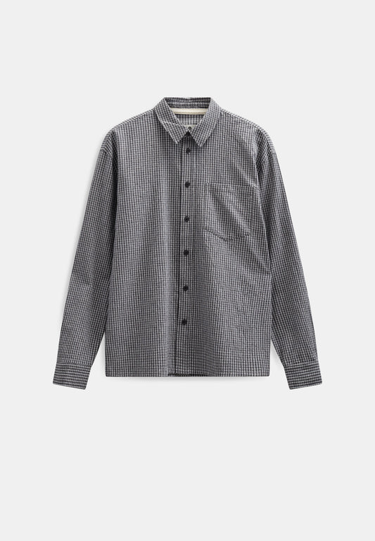 Vista frontale flat lay della Anerkjendt AKOTTO Small Check LS Shirt in colorazione Black Grey: camicia uomo a micro quadri grigio scuro e antracite con colletto classico bottoni scuri tasca a toppa sul petto e polsini con etichetta Anerkjendt visibile su sfondo grigio chiaro