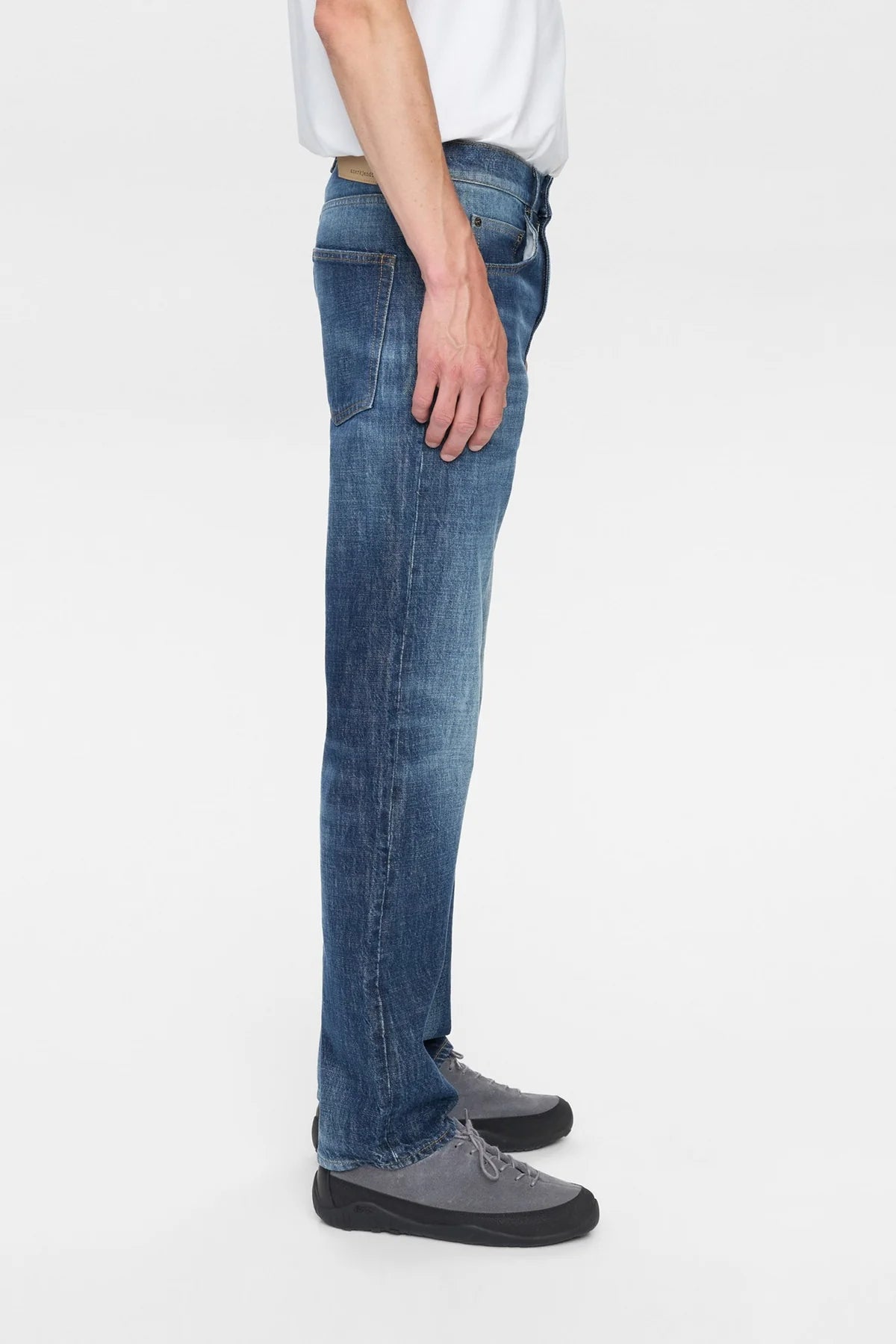 Dettaglio ravvicinato della tasca anteriore destra e della vita dei jeans Anerkjendt AKJUSTIN Dark Blue Sky: primo piano del denim blu medio con texture jacquard all-over lettera A in rilievo tono su tono chiusura a bottone argento e passante cintura su sfondo bianco