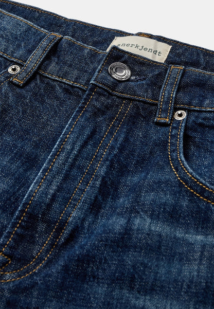 Vista frontale ravvicinata dei jeans Anerkjendt AKJUSTIN 8016 Dark Blue Sky indossati dal modello: zoom su vita e cosce con denim blu medio lavaggio vintage, texture jacquard all-over con pattern lettera A in rilievo, cintura con passanti e chiusura a bottone metallico argento