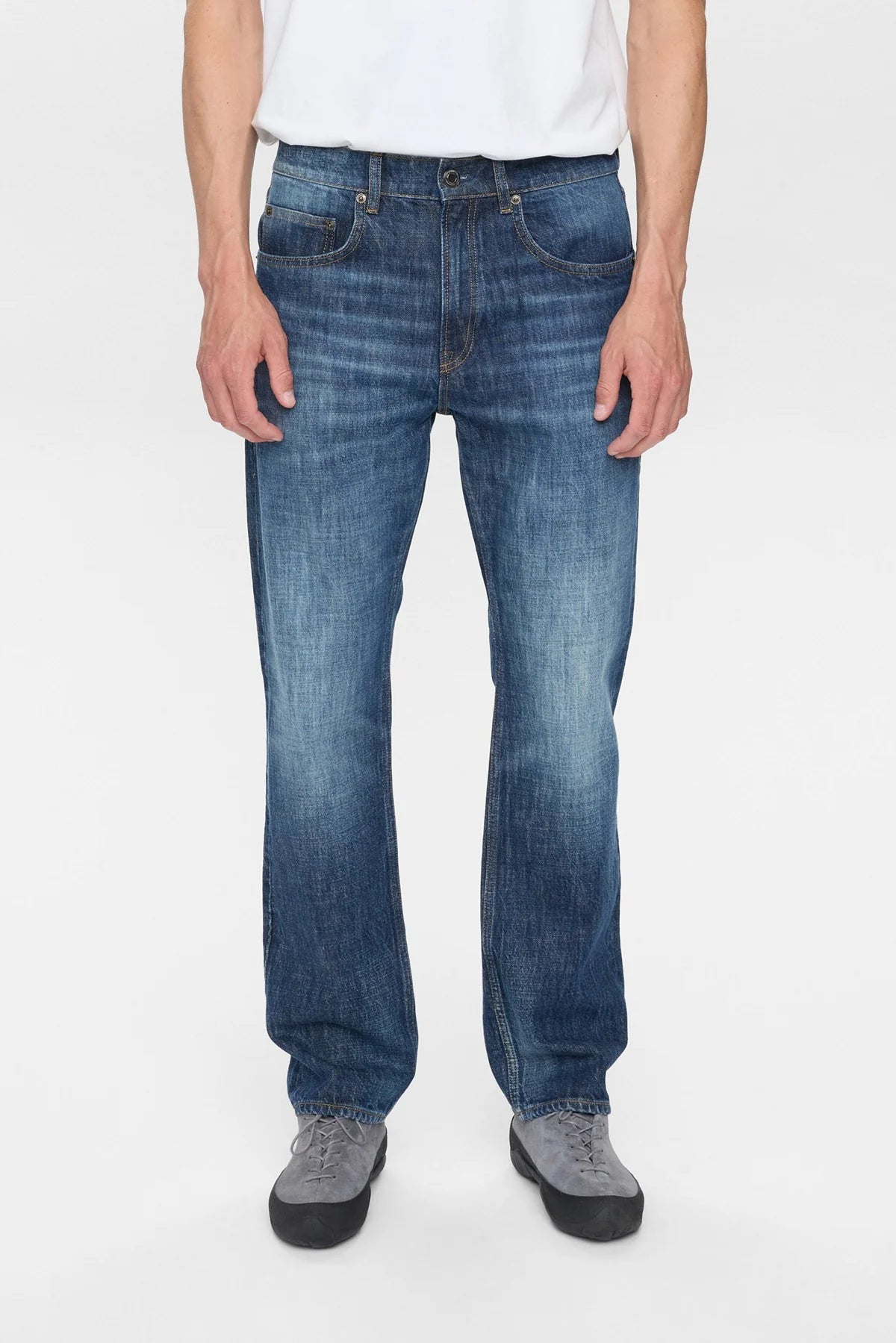 Vista posteriore intera del modello che indossa i jeans Anerkjendt AKJUSTIN Dark Blue Sky con t-shirt bianca oversize e scarpe nere: retro dei jeans straight fit con due tasche posteriori arcuate, patch etichetta beige Anerkjendt e texture jacquard all-over su sfondo bianco