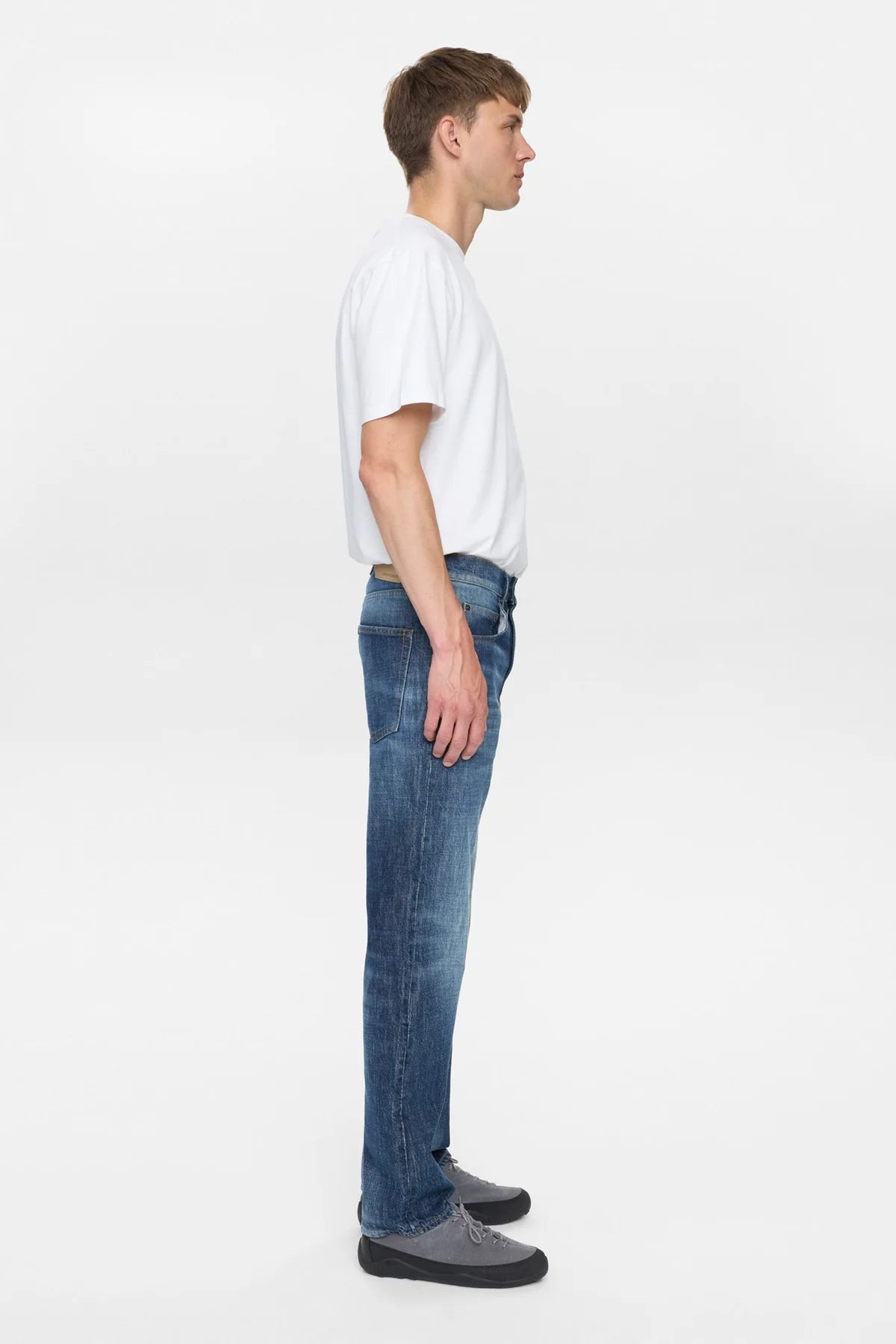 Vista frontale flat lay dei jeans Anerkjendt AKJUSTIN 8016 Dark Blue Sky su sfondo grigio chiaro: jeans uomo straight fit in denim blu medio scuro con texture jacquard all-over pattern lettera A tono su tono 5 tasche passanti cintura e bottone metallico argento